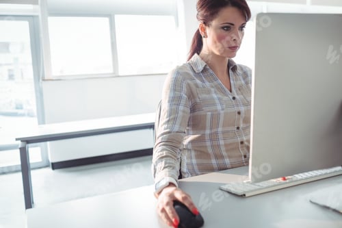 Preview: Woman wearing plaid shirt sitting at office desk using computer near windows, bench, copy space