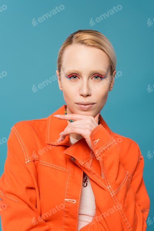 Preview: portrait of blonde woman with colorful makeup wearing orange jacket and looking at camera isolated