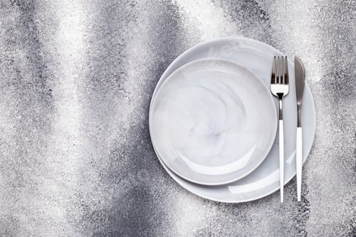 Preview: Two empty ceramics plates and unused knife with fork, crockery on a gray grunge table