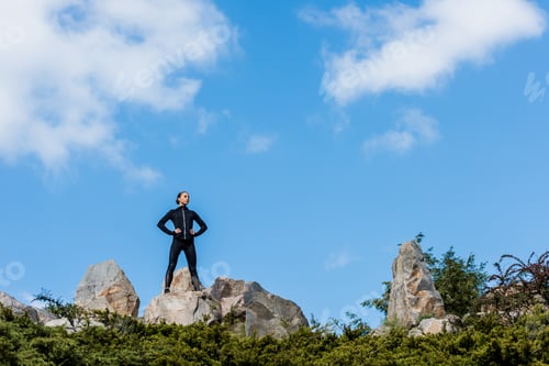 Preview: young woman standing on rocks with arms akimbo and looking away