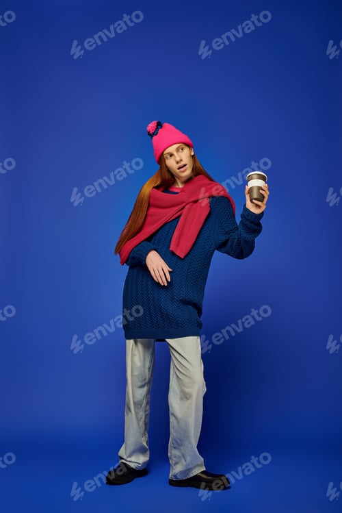 Preview: Young man expresses emotions in vibrant blue backdrop while holding a coffee cup