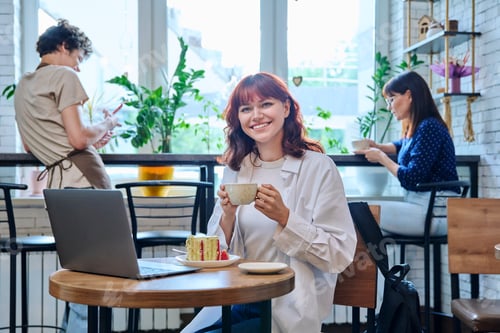 Preview: Female college student with laptop in cafe, with cup of coffee, piece of cake