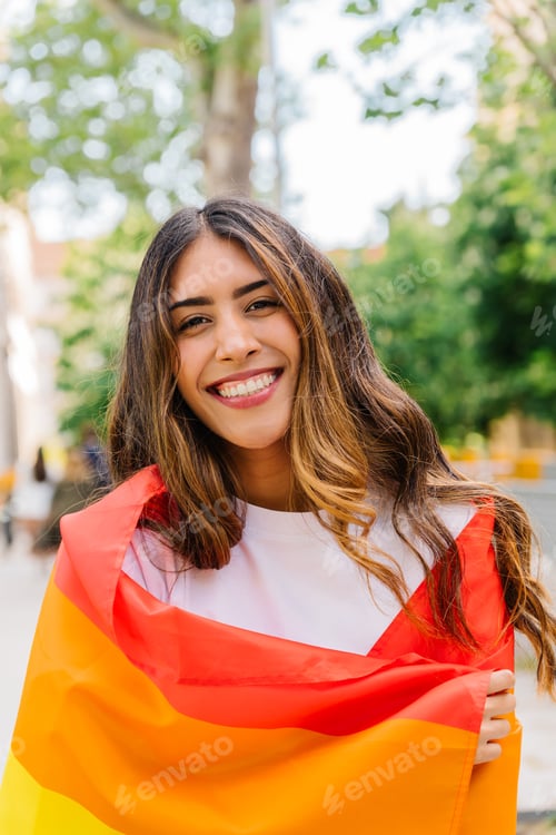 Preview: Young latin woman embracing rainbow flag in urban park during pride month