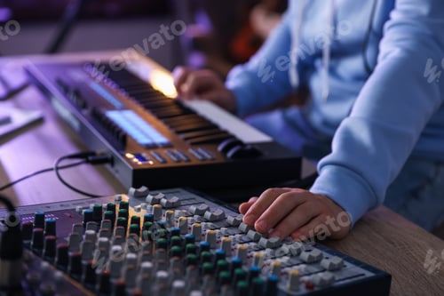 Preview: Man working with MIDI keyboard and dj mixer at wooden table in home studio, selective focus