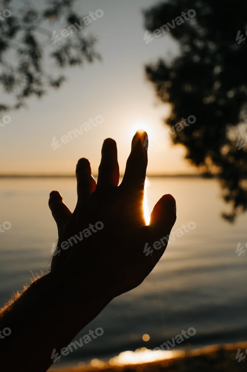 Preview: Man reaching for sun, outdoors. Close-up of hand on background of sunset and lake in nature.