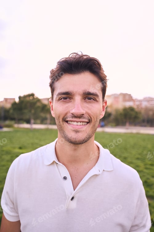 Preview: Vertical portrait of attractive smiling young man looking at camera in park. Caucasian male handsome