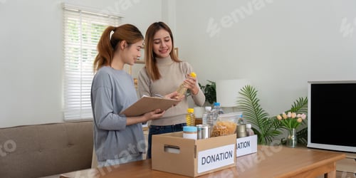 Preview: Donation and two woman volunteer asian of happy packing food in box at home. Charity