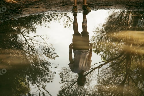 Preview: Upsidedown reflection of a person in a tranquil water puddle amidst nature.