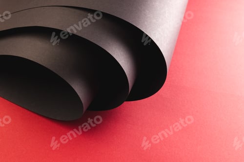Preview: Close up of rolled up pieces of black paper with copy space on red background