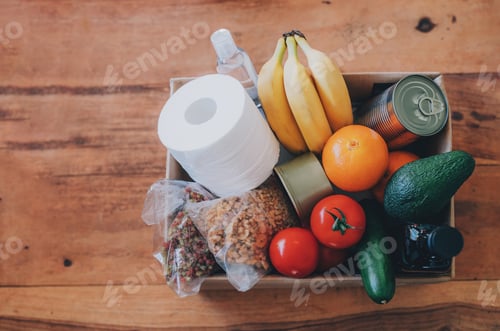 Preview: Box with food, toilet paper and hand sanitizer on the wooden table. Flat lay.