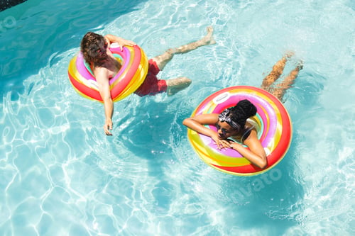 Preview: A diverse couple, a young African American woman and a Caucasian man relax on colorful pool floats