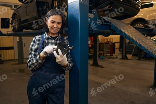 Preview: Cheerful female mechanic looking at her smartphone