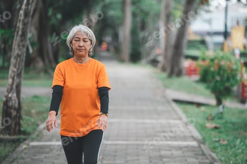 Preview: white-haired elderly person exercising in the park early in the morning.