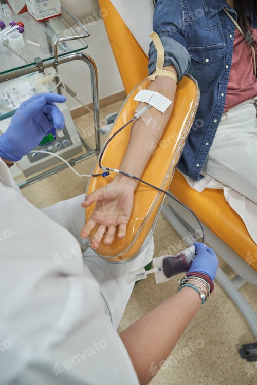 Preview: Crop nurse in scrubs performing blood donation on anonymous woma
