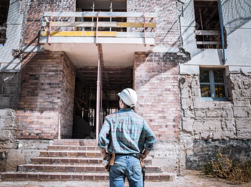 Preview: A mason observing the building under construction where he works.