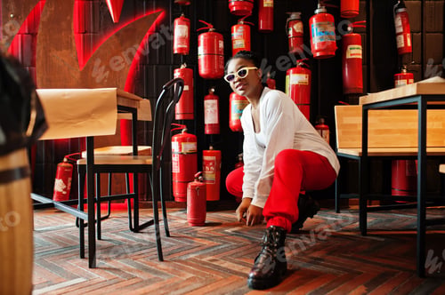 Preview: African woman posed against wall with old extinguisher.