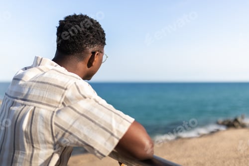 Preview: Rear view of pensive african american man relaxing looking at the ocean. Copy space.