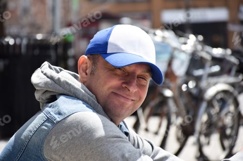 Preview: Portrait of happy middle aged man sitting on a curb looking into camera smiling