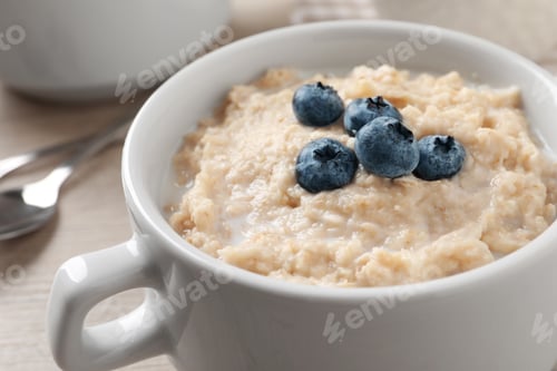 Preview: Tasty oatmeal porridge with blueberries in bowl on table, closeup