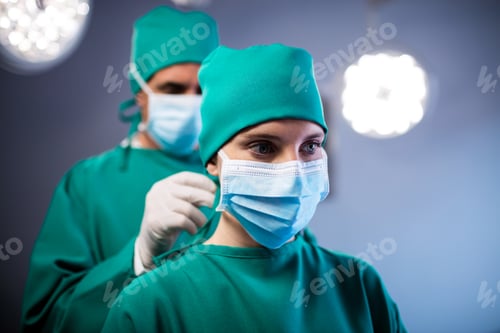 Preview: Surgeon helping a nurse in tying surgical mask in operation room