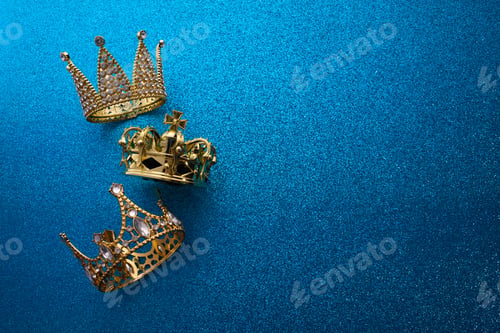 Preview: Epiphany Day or Dia de Reyes Magos concept. Three gold crowns on blue sparkling background