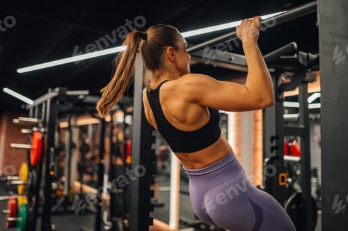 Preview: Determined sportswoman performing pull ups in modern gym setting