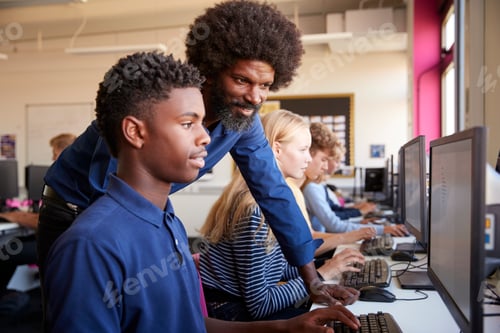 Preview: Teacher Helping Teenage Male High School Student Working In Computer Class