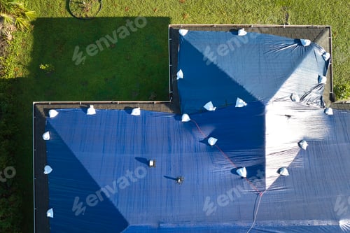 Preview: Aerial view of damaged in hurricane Ian house roof covered with blue protective tarp