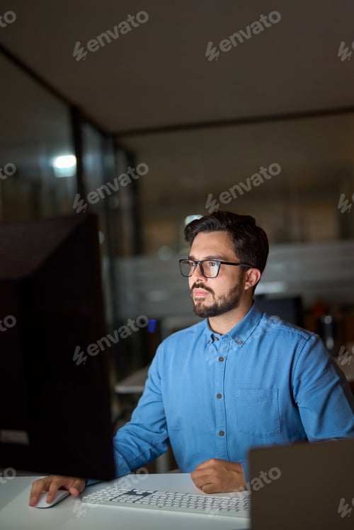 Preview: Busy young business man using computer working late in office. Vertical.
