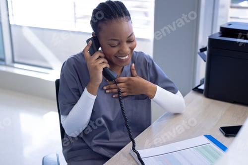 Preview: Happy african american female doctor talking on phone in hospital reception