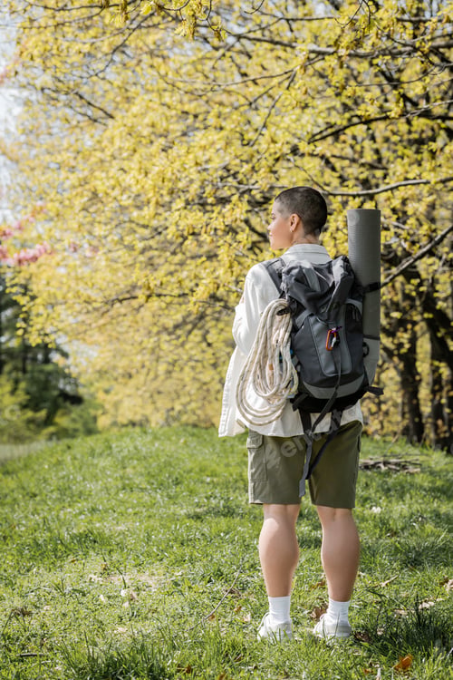 Preview: Side view of young and short haired female tourist with backpack, climbing rope and fitness mat
