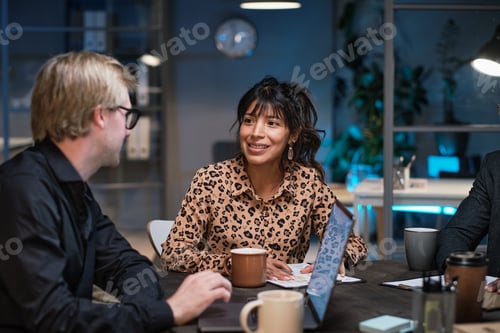 Preview: Young businesswoman sitting at the table working with documents and discussing with colleagues