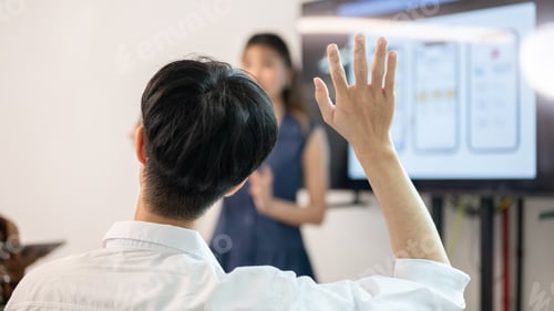 Preview: Man raised hand asking question to woman speaker standing in front of monitor screen in meeting room