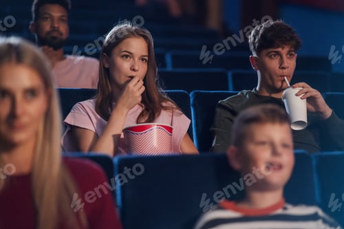 Preview: Front view of cheerful young couple with drink and popcorn in the cinema, watching film