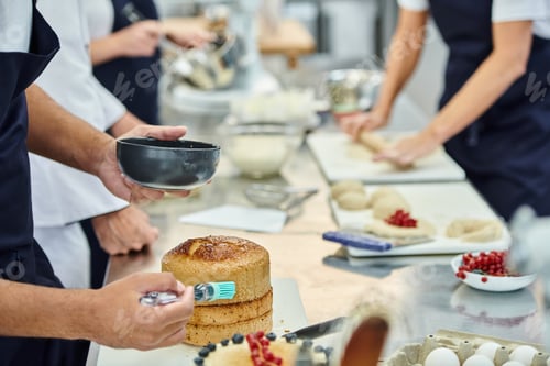 Preview: cropped view of african american chef using silicone brush on cake next to blurred colleagues