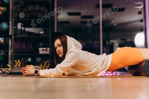 Preview: Muscular young athletic woman with perfect beautiful body in sportswear using foam roller massager