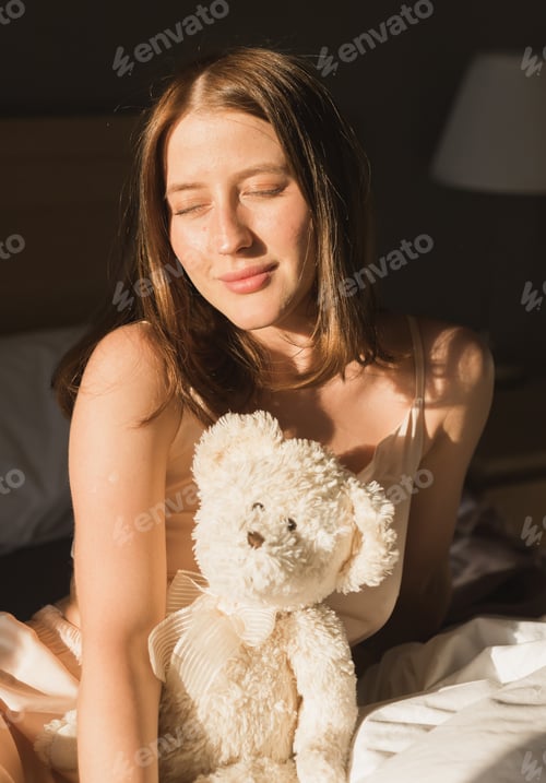 Preview: Girl is waking up in morning stretches in bed and sun shines from the window. Happy young woman