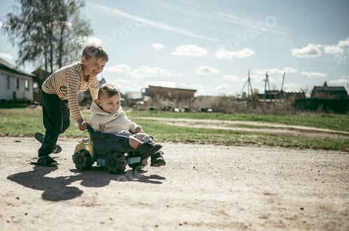 Preview: The boy rides his younger brother's toy car. Summer in the village
