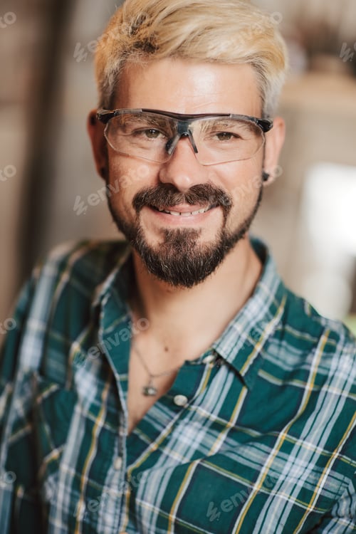 Preview: Portrait of happy young hipster bearded man by profession carpenter in the workshop.