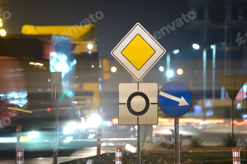 Preview: Roundabout road signs with blurred cars on city street traffic at night.