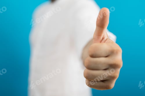 Preview: Closeup of a person doing the thumbs-up gesture under the lights on a blurry background