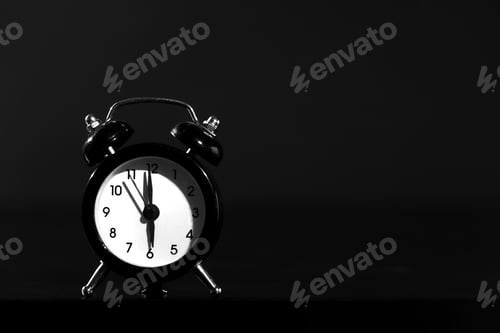 Preview: Black old style alarm clock isolated on black background. close-up