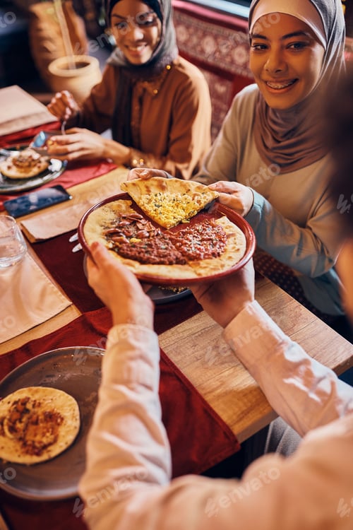 Preview: Young Muslim woman and her friends eating Turkish pizza for lunch.