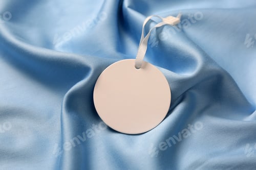 Preview: Blank white tag on light blue silky fabric, closeup. Space for text