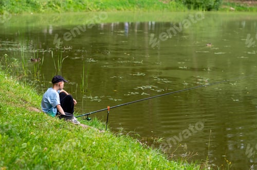 Preview: Boy fishing alone on pond shore in summer landscape