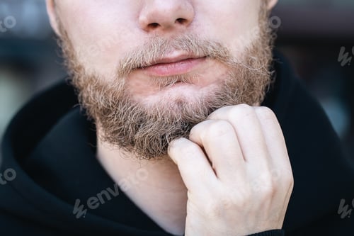 Preview: Close-up, a young man touches his beard with his hand.