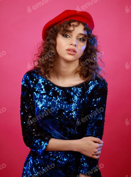 Preview: Adorable curly-haired girl wearing hat and gilded dress and standing on pink background