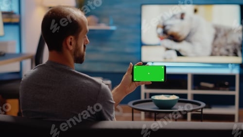 Preview: Young man watching horizontal green screen on smartphone