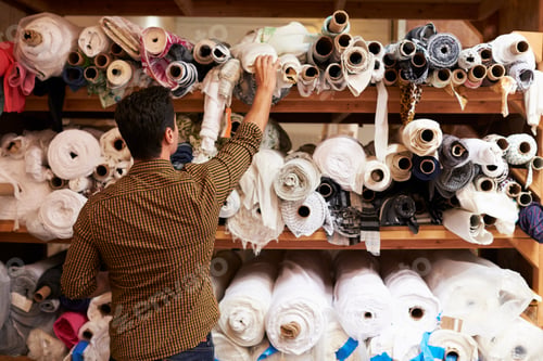 Preview: Man reaching to select fabric from storage shelves