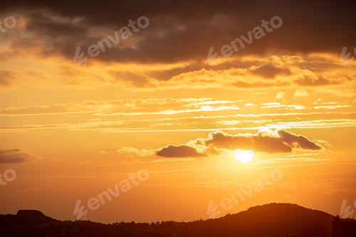 Preview: Beautiful sunset on sky. Gold sun lightens the clouds over mountains.